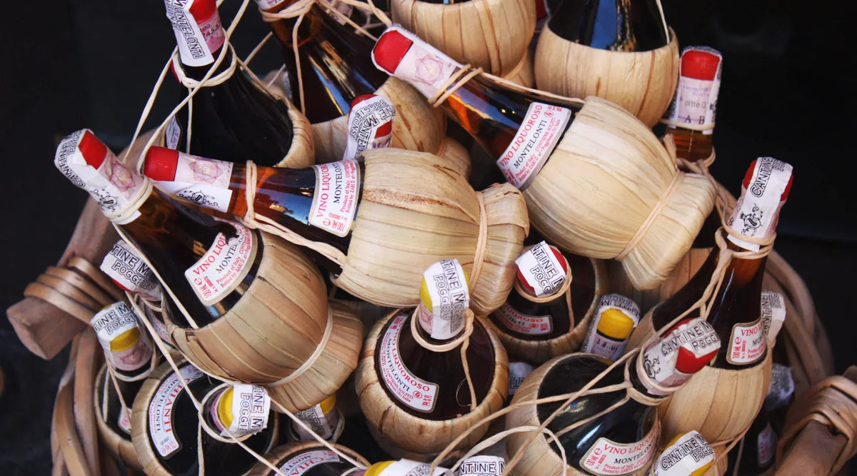 Bouteilles traditionnelles de vin Chianti enveloppées de paille dans un panier, symbolisant l’artisanat et l’authenticité des vins toscans.